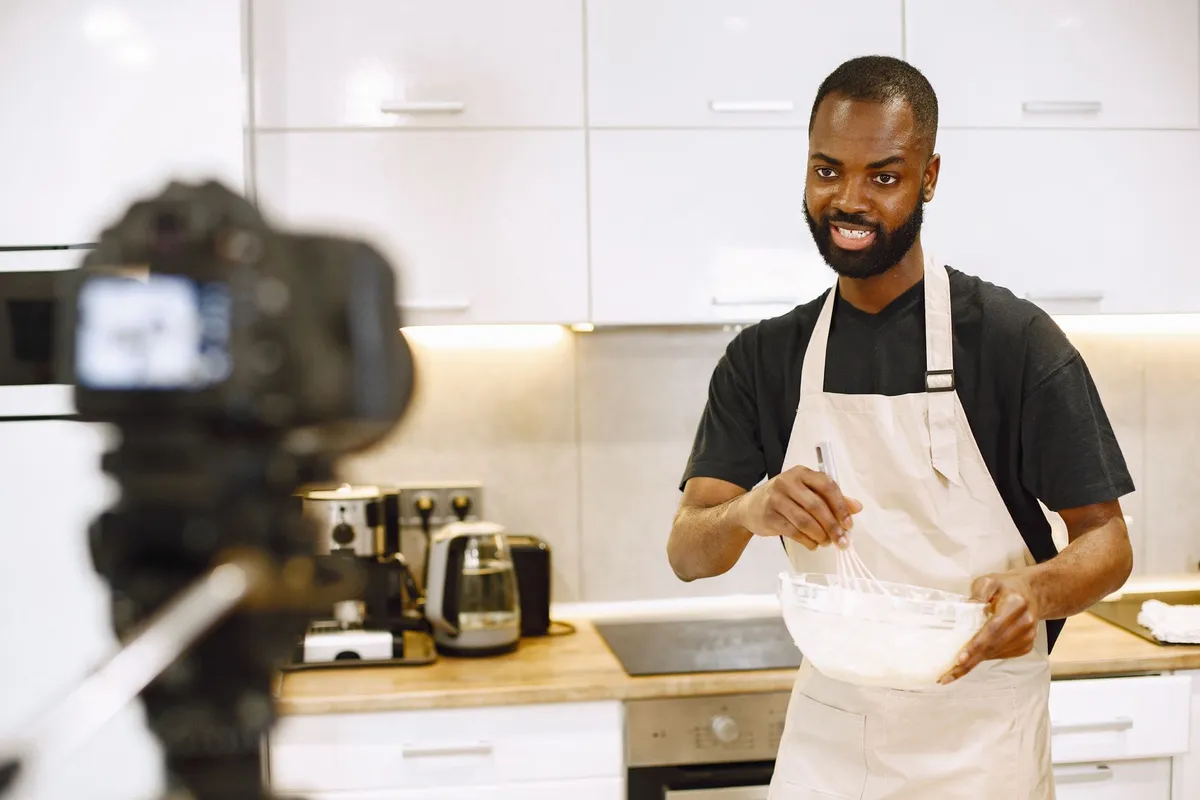 Main versant de la pâte à beignets dans un bol, atelier de pâtisserie afro à Paris