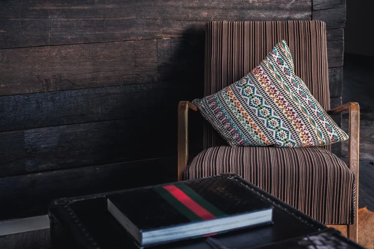 Coin lecture cosy dans un petit appartement : fauteuil en rotin, coussins wax colorés, étagère de livres et lampe chaude près d'une fenêtre