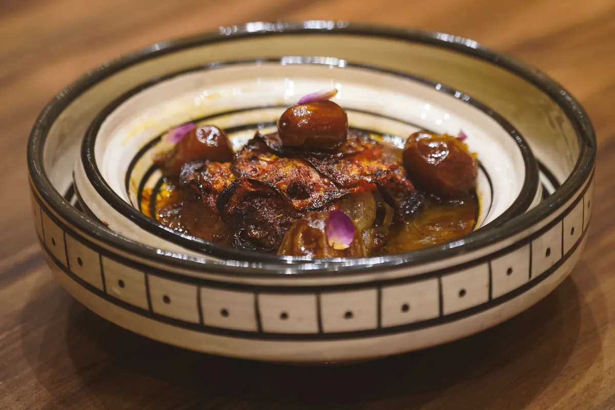 Grand plat de thiéboudienne mauritanien servi sur une table basse avec du thé à la menthe, ambiance chaleureuse d'un restaurant parisien de la diaspora africaine