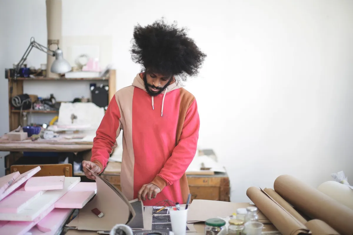 Mains d'un artisan maroquinier afro travaillant une pièce de cuir sur mesure dans son atelier parisien