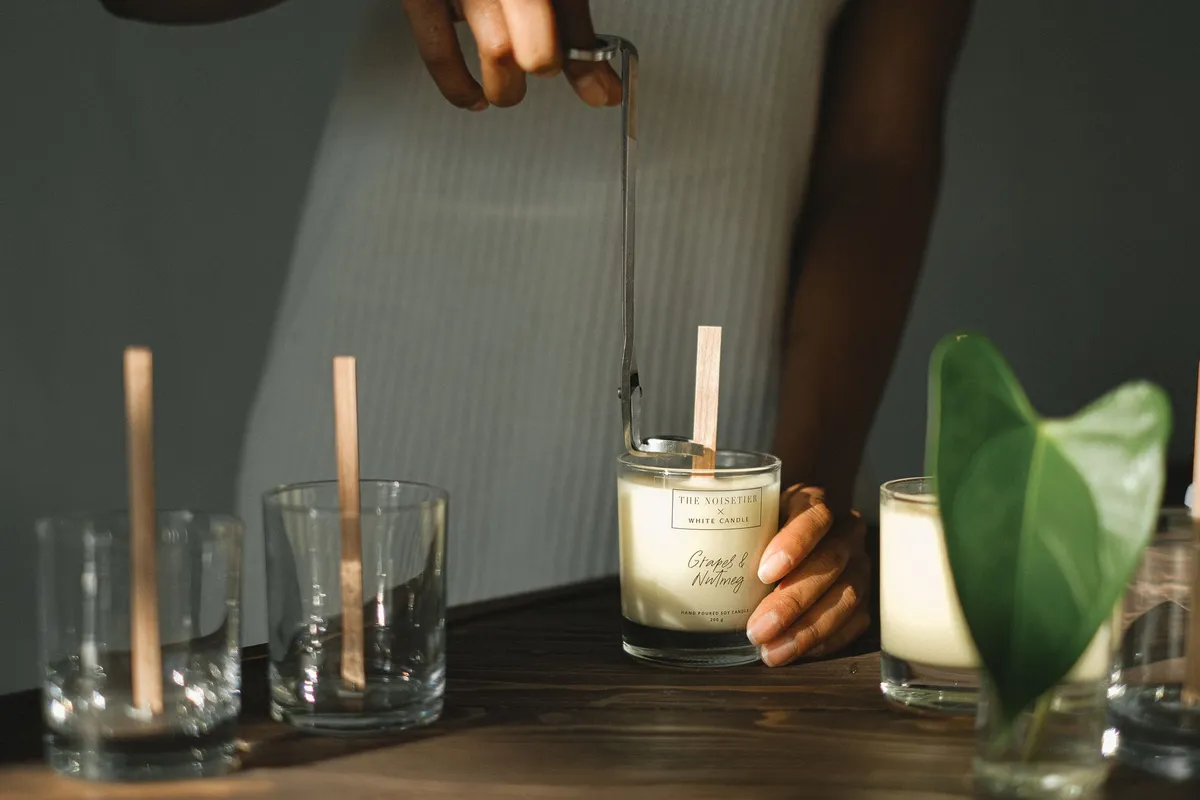 Artisan afro versant de la cire végétale dans un pot en céramique pour créer une bougie artisanale dans son atelier parisien