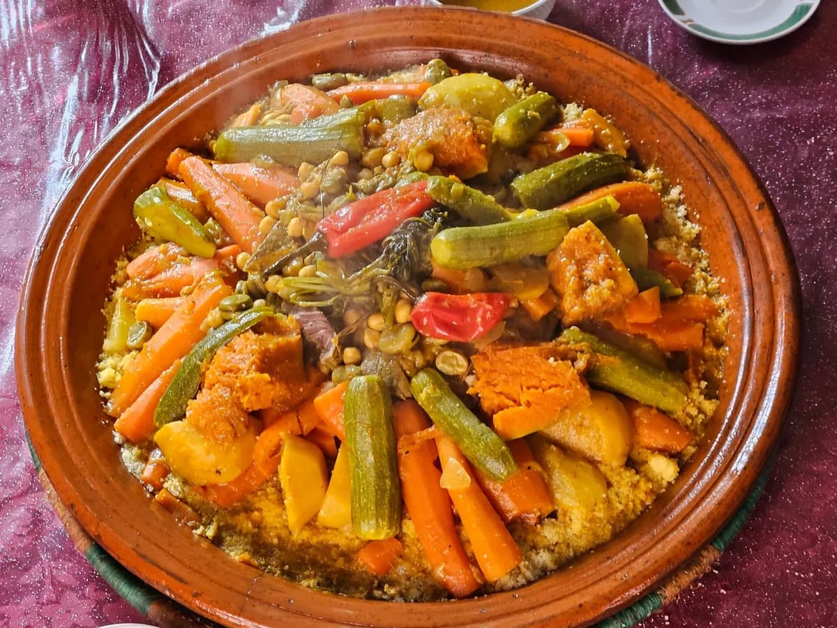 Grand plat de couscous mauritanien traditionnel garni de légumes colorés et de viande mijotée, servi sur une nappe à motifs africains