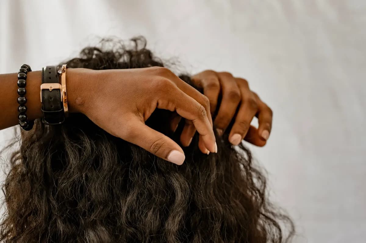 Femme aux cheveux crépus naturels hydratés et brillants, appliquant un soin sur ses boucles devant un miroir